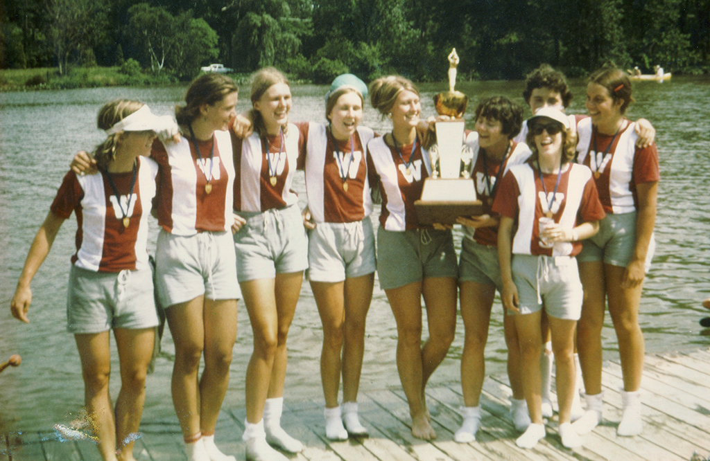 The members of the UW varsity eight boat standing on a pier holding their trophy.