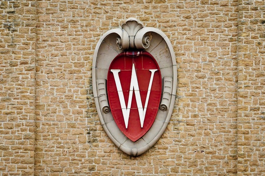 An architectural element in the shape of a crest with a white W on red center against the brick wall of the Field House.