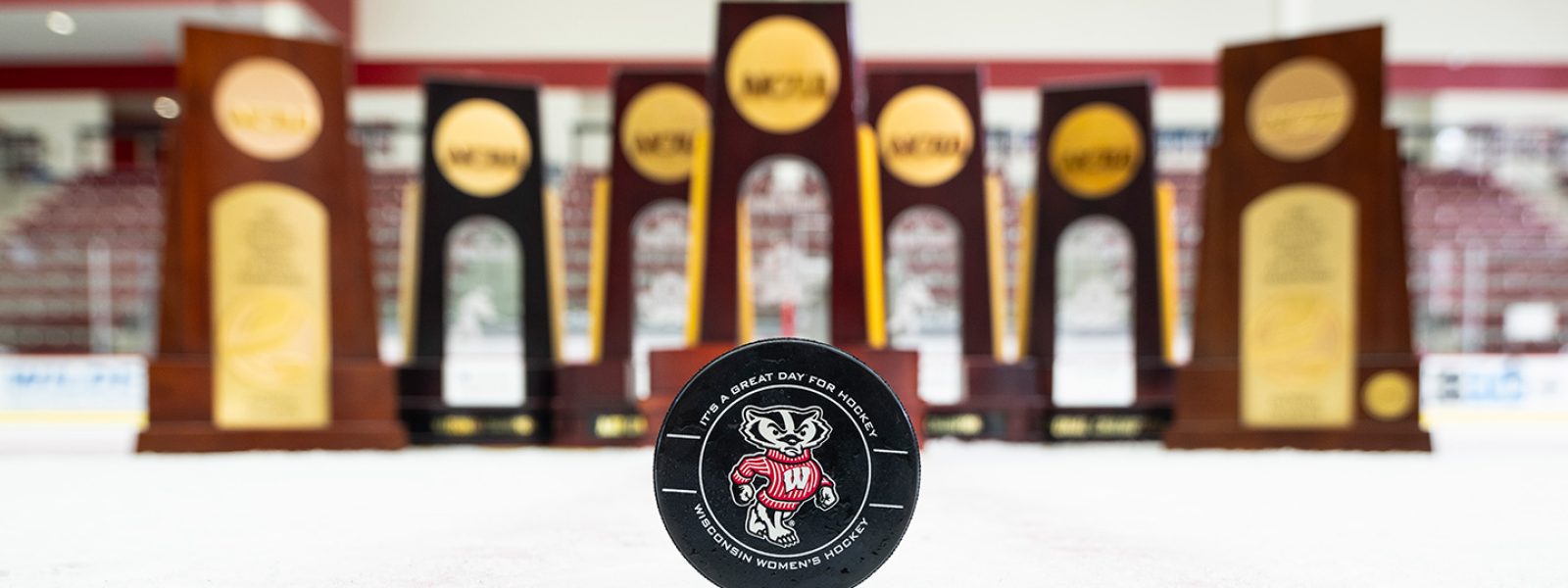 A hockey puck with Bucky Badger is displayed in front of seven hockey trophies.