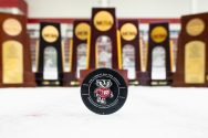 A hockey puck with Bucky Badger is displayed in front of seven hockey trophies.