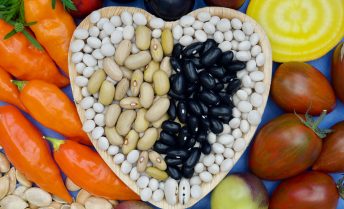 Dry beans are artfully arranged in the shape of a heart surrounded by vegetables
