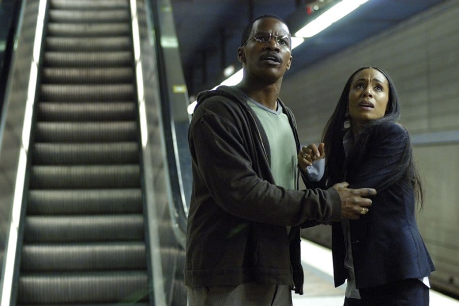 Still frame from the movie Collateral showing actors Jamie Foxx and Jada Pinkett Smith looking panicked in a subway station, next to an escalator.