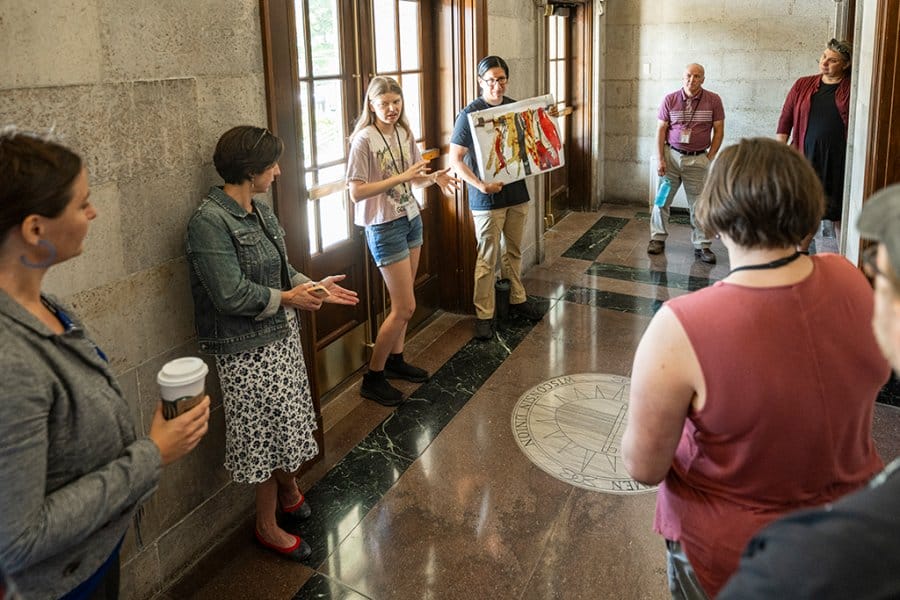 Tour guides, with the help of a visual, explain the inlaid art in the upper entrance to the Memorial Union to a group of people.