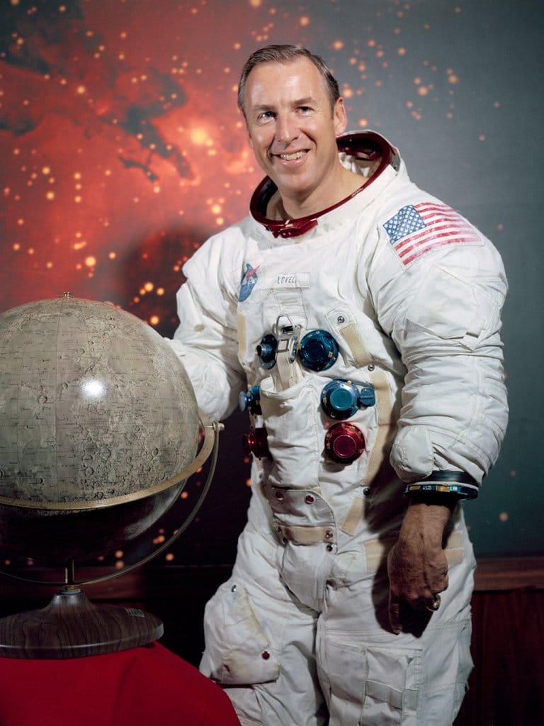 Astronaut Jim Lovell dressed in his space suit next to a globe of the moon. 
