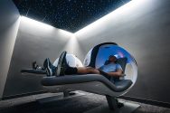 Two students nap in nap pods in a room with a starry sky.
