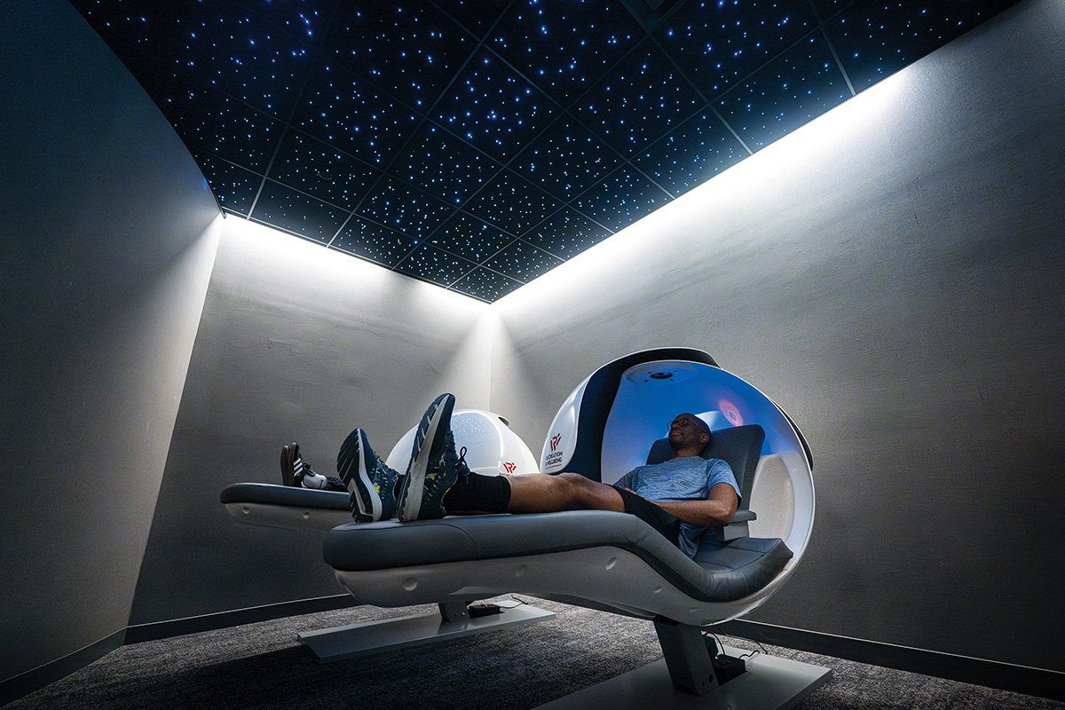 Two students nap in nap pods in a room with a starry sky.