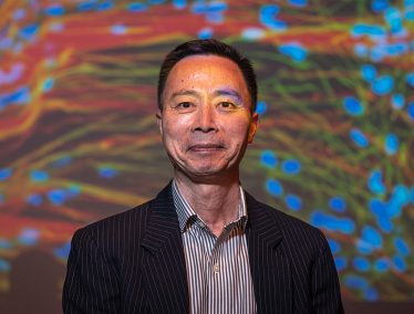 Su-Chun Zhang standing in front of a projected image of brightly colored neurons and glial cells.