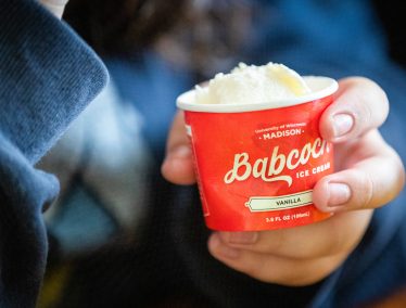 Person's hand holding a red paper dish of Babcock vanilla ice cream