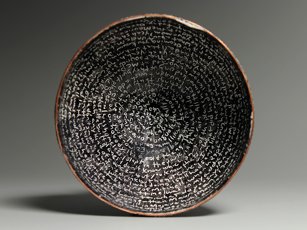 The interior of a bowl which has white text on black enamel, written in a circular manner.
