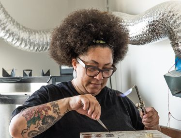 Holding a blow torch, Tanya Crane works on small pieces of metal in her studio.