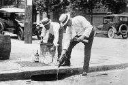 Black and white photograph of two men pouring whiskey down a street gutter.
