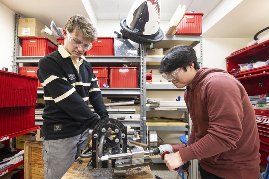 Two students wearing safety glasses work on a machine