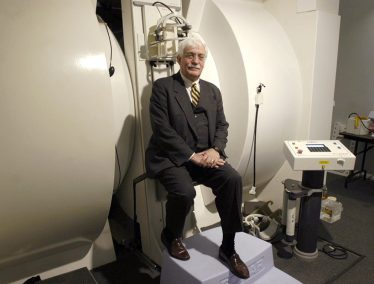 Raymond Damadian wearing a suit poses in front of an MRI machine