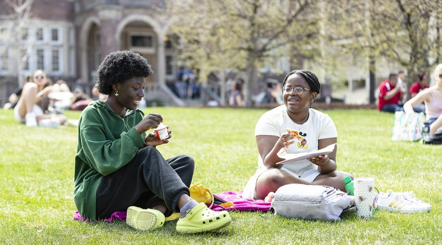 Two students eat lunch together on the Library Mall lawn