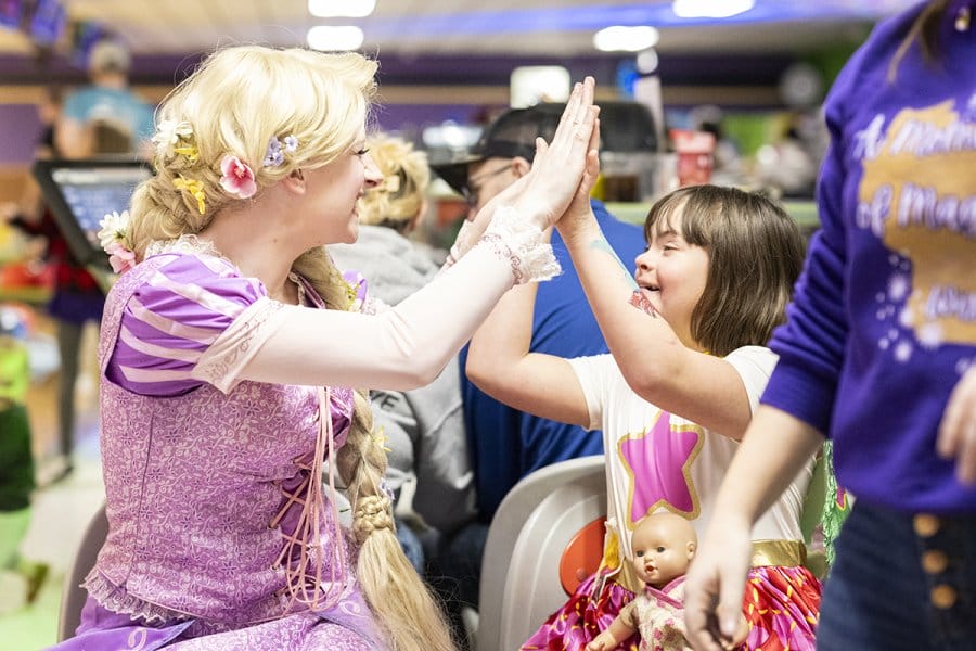 A woman dressed as a princess plays with child also dressed as a princess