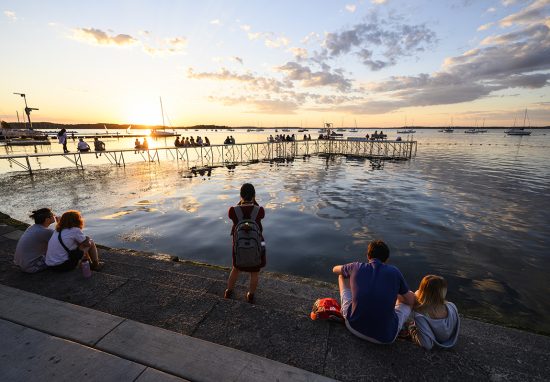 People on the shore of Lake Mendota take in a summer sunset
