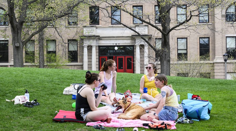 Four women and a dog lounge on blankets on Bascom Hill outside of the Education building