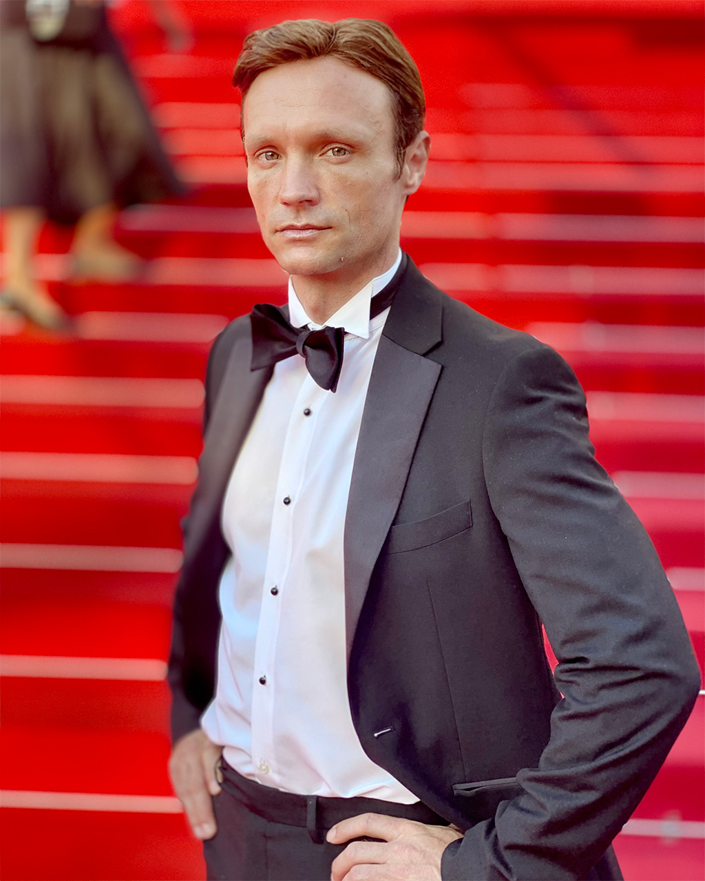 Hans Obma, wearing a tuxedo, poses on the red carpet.