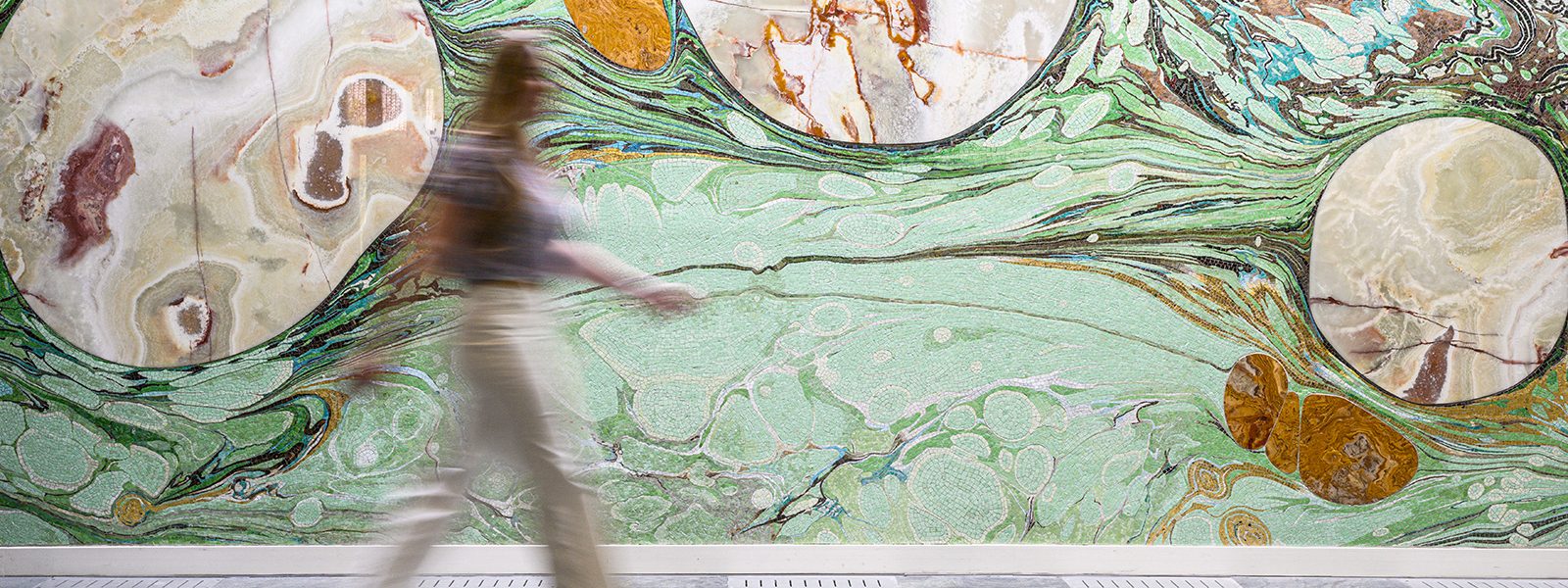 A person walks in front of a large, marbled mosaic.