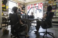 Three students sit in front of microphones in radio station