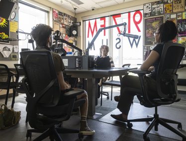 Three students sit in front of microphones in radio station