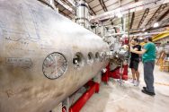 Two research fellows check a component on a large metal cylinder