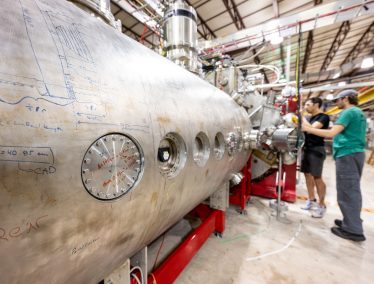 Two research fellows check a component on a large metal cylinder