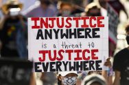 Amid a crowd of protesters, a sign reads "Injustice anywhere is a threat to Justice Everywhere"