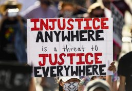 Amid a crowd of protesters, a sign reads "Injustice anywhere is a threat to Justice Everywhere"