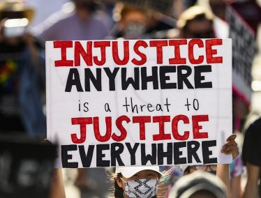 Amid a crowd of protesters, a sign reads "Injustice anywhere is a threat to Justice Everywhere"