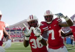 Badger football players smile and flash the 'W' sign on the sidelines of a game at Camp Randall