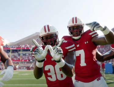 Badger football players smile and flash the 'W' sign on the sidelines of a game at Camp Randall