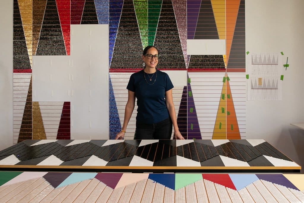 Dyani White Hawk stands with her large-scale, colorful work in an art studio.