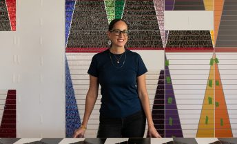 Dyani White Hawk stands with her large-scale, colorful work in an art studio.