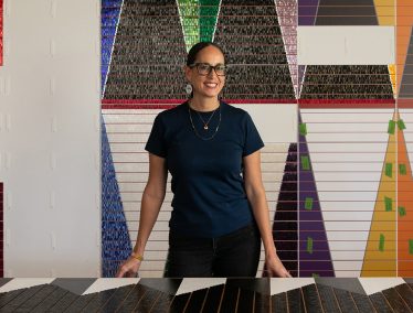 Dyani White Hawk stands with her large-scale, colorful work in an art studio.