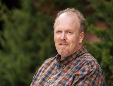 Headshot of Gary Grosklaus outdoors, wearing a plaid shirt.