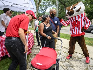 People wearing Badger gear and name tags interact with a friendly Bucky Badger mascot