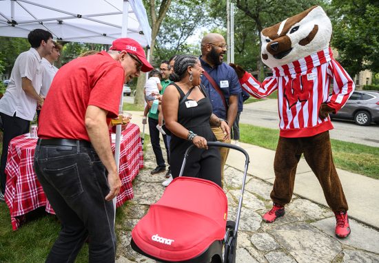 People wearing Badger gear and name tags interact with a friendly Bucky Badger mascot