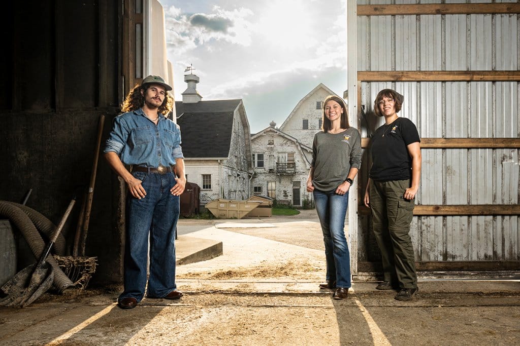 Three students pose in a barn.