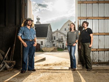 Three students pose in a barn.