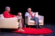 Mike Leckrone and Doug Moe converse sitting in armchairs on a stage