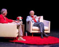 Mike Leckrone and Doug Moe converse sitting in armchairs on a stage