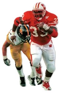 Photo cutout of Ron Dayne rushing with the football being pursued by an opposing player