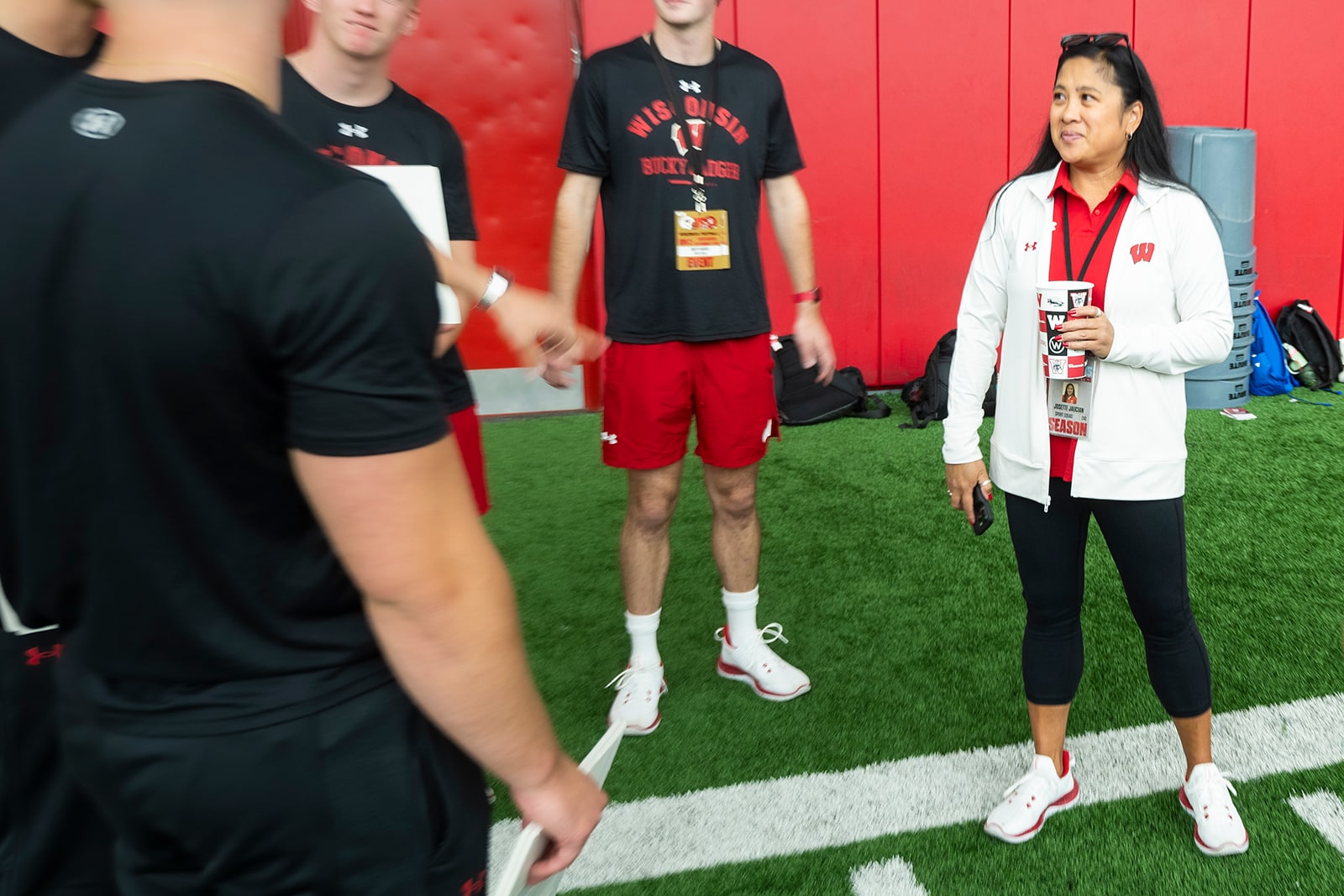 A group of students in athletic attire stand on an indoor turf field next to Josette Jaucian.