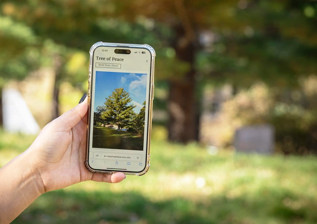 A cell phone is held in front of a tree on campus; the screen displays information about the tree as part of a virtual tour.