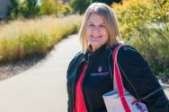 Erin Warner, wearing a UW Off-Campus Housing Services jacket and holding a Wisconsin Mom canvas tote bag.