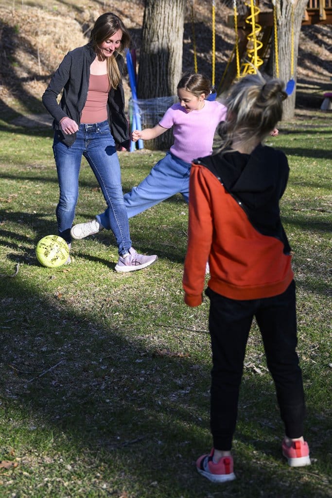 Calarco kicking a soccer ball around on a grassy field with her two children.