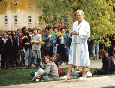 A group of people gathered outdoors on Bascon Hill, with Rodney Dangerfield (as character Thornton Melon) in a bathrobe and slippers among casually dressed students and actors.