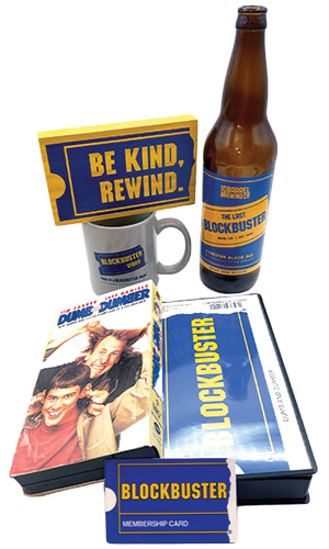 A collection of Blockbuster-themed items including a beer bottle labeled 'The Last Blockbuster,' a Blockbuster logo mug, a 'Dumb and Dumber' VHS tape, a membership card, and a sign reading 'Be Kind, Rewind.'