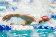 A swimmer wearing a red swim cap is swims freestyle stroke in a pool, with water splashing around and lane lines visible on either side of her.